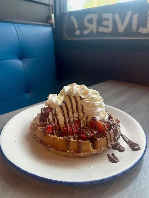A waffle with whipped cream and chocolate in a blue booth