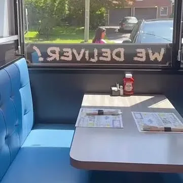 A blue booth by the window, the We Deliver sign reversed on the glass